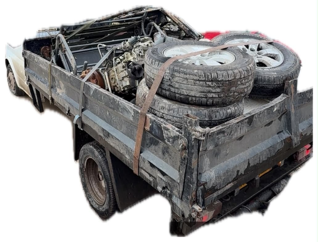 White pickup truck loaded with scrap metal, engine parts and stacked used tires for scrap collection